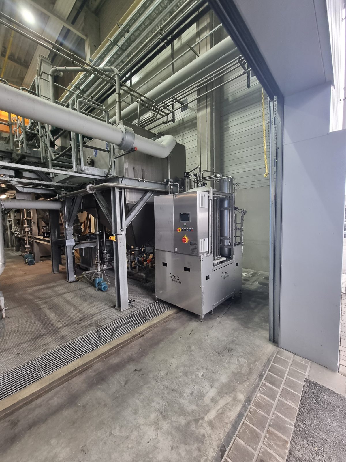 Atec Miditube Membranfiltrationsanlage aus Edelstahl mit Bedienpanel am Schaltschrank, aufgestellt in einer hohen Produktionshalle zwischen Stahlbühnen und Rohrleitungen.