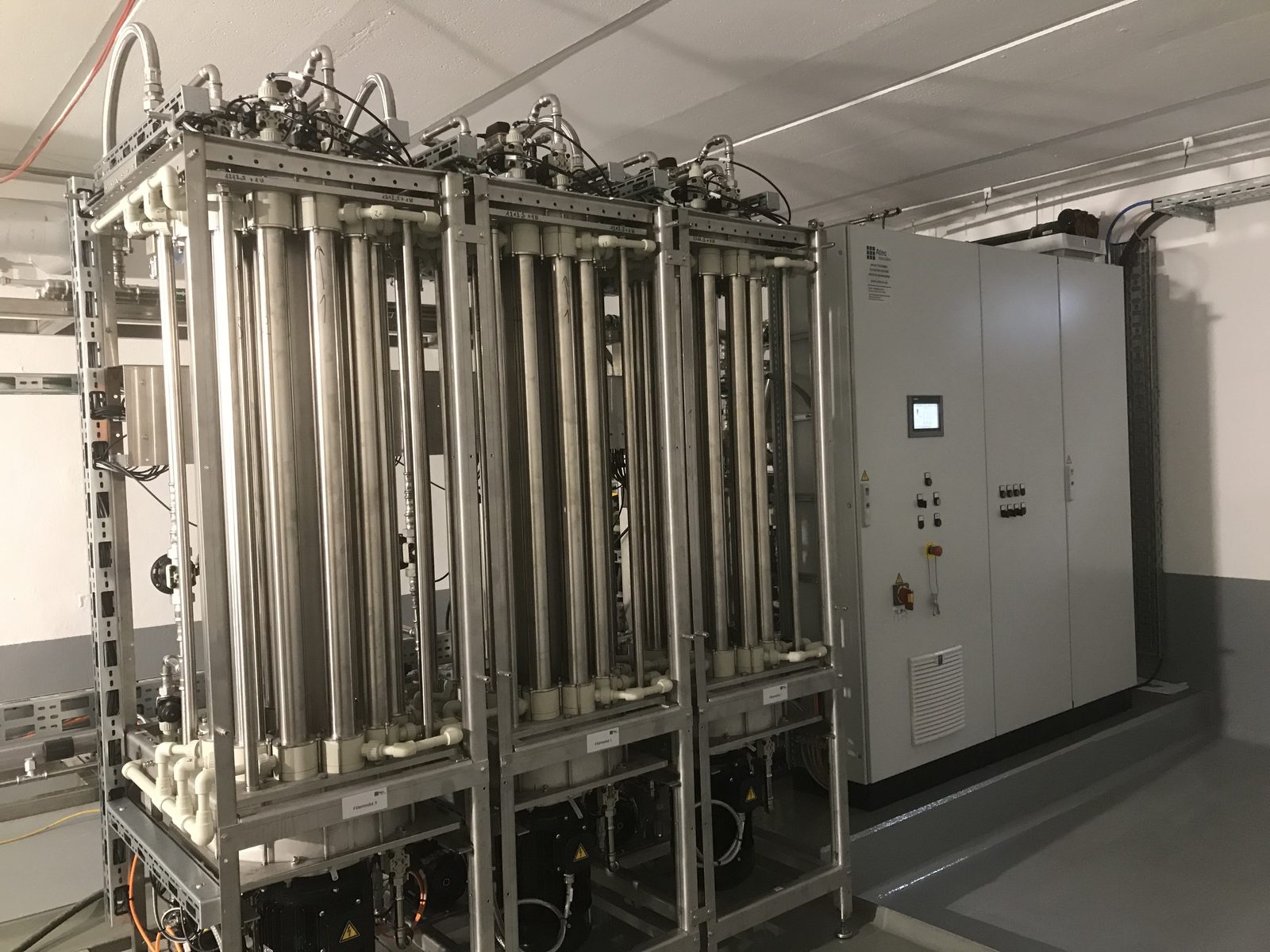 Drei Atec Miditube Filtermodule nebeneinander; in jedem Rahmen stehen die Membrangehäuse senkrecht und parallel. Rechts der Schaltschrank mit Bedienpanel.