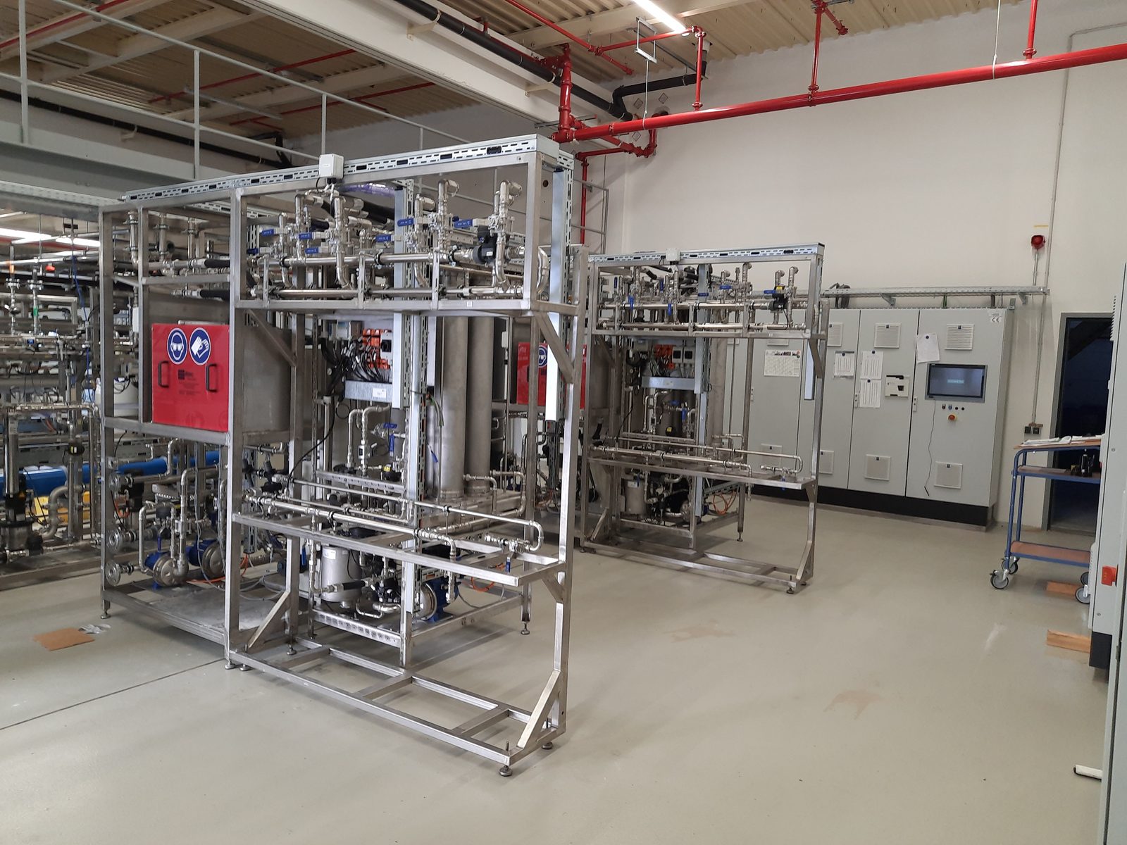 Zwei Atec Miditube Cross-Flow-Filtrationsanlagen in Edelstahlrahmen in einer hellen Industriehalle, dahinter die Schaltschränke.